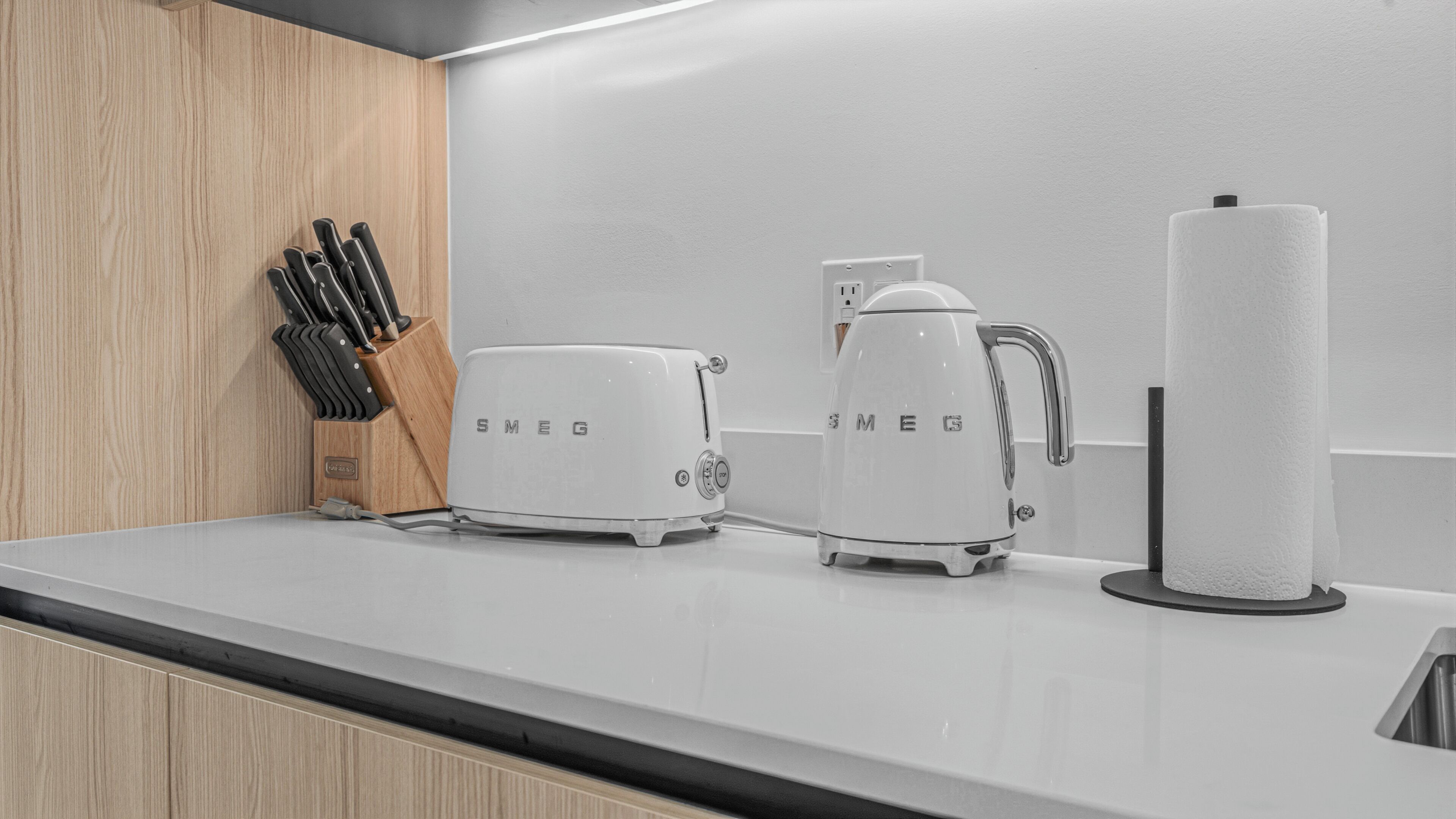 A kitchen with a wooden countertop, a knife block, a Smeg toaster, a Smeg kettle, and a roll of paper towels.