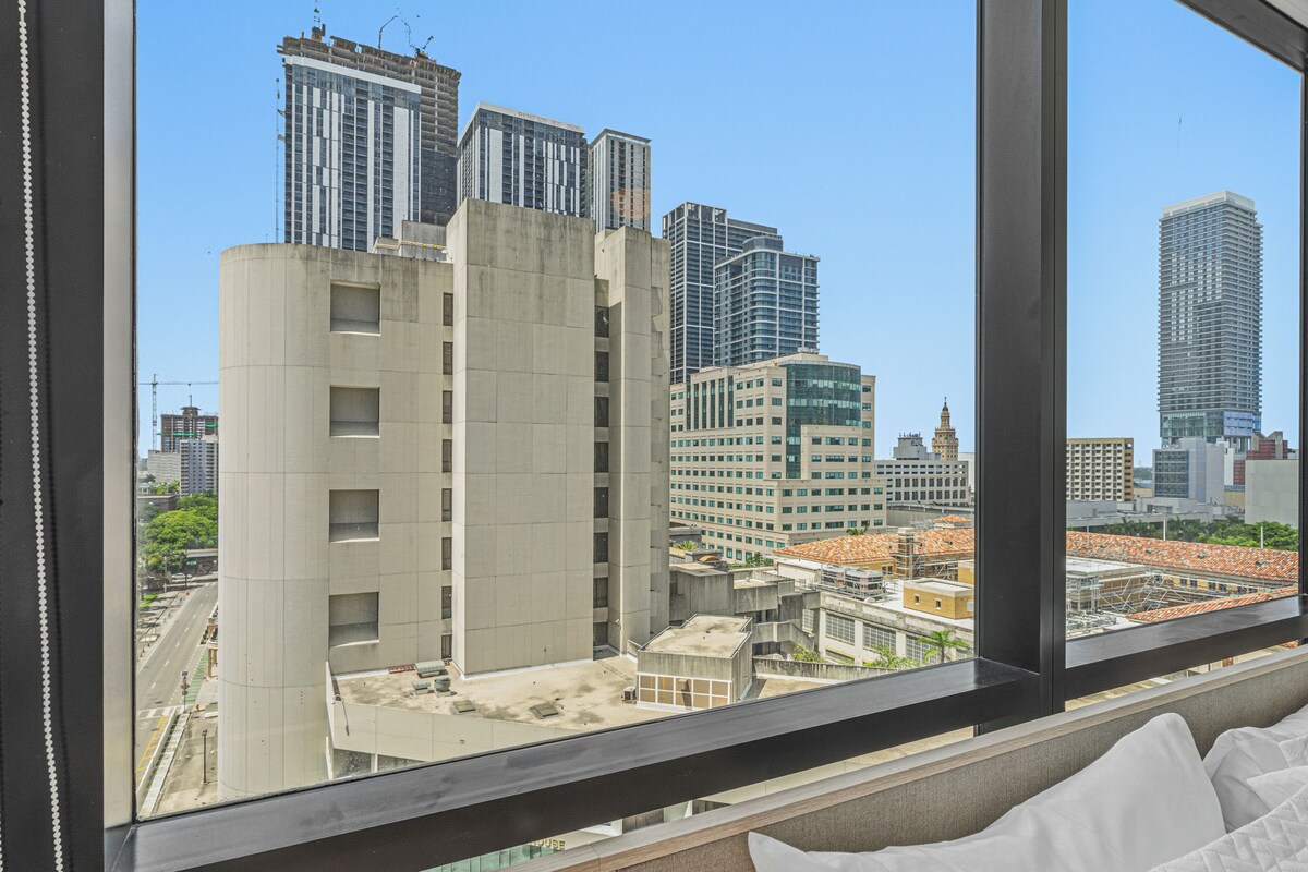 A hotel room with a large window overlooking a cityscape with various buildings.