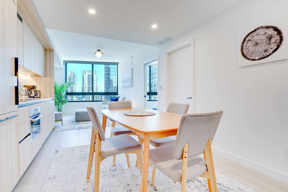 A modern kitchen with a dining area, large windows, and a view of high-rise buildings.