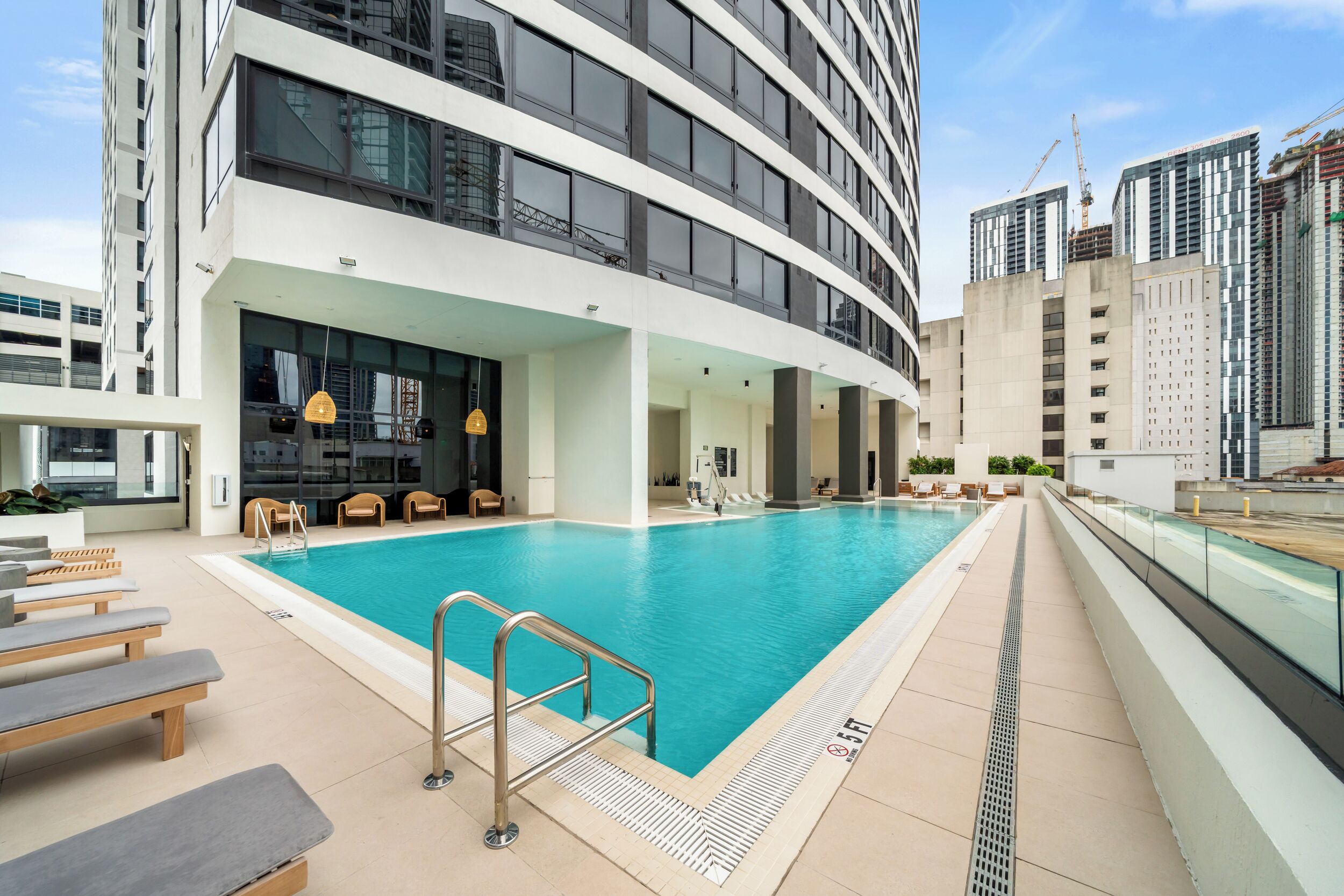 Un hotel moderno con piscina infinita en la azotea, mobiliario de exterior y vistas de edificios altos circundantes.