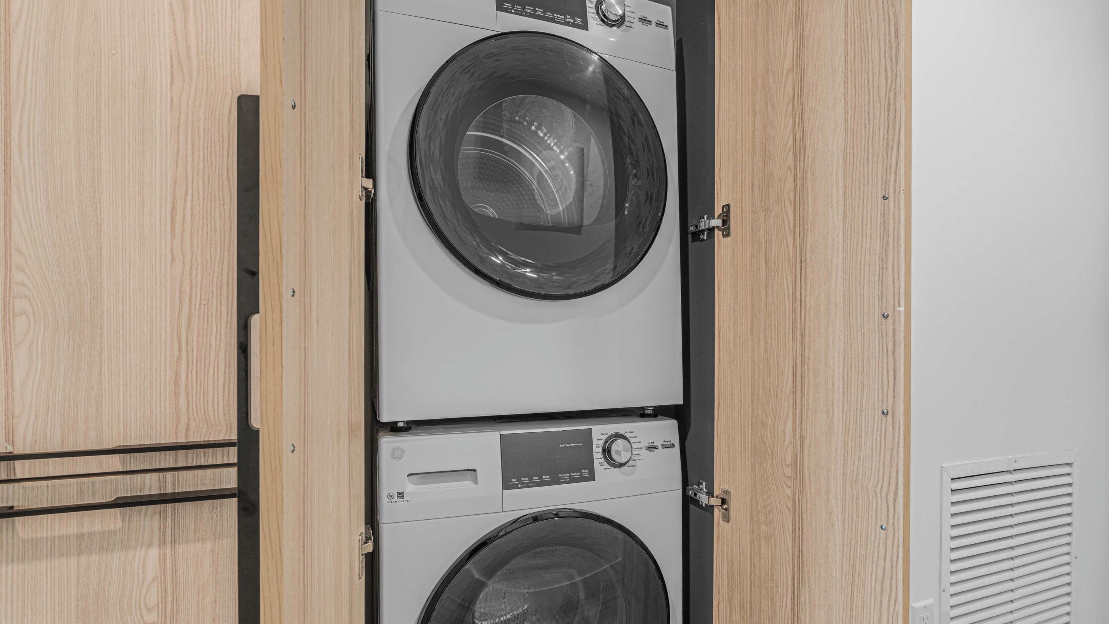 A stacked washer and dryer unit with a wooden cabinet door.