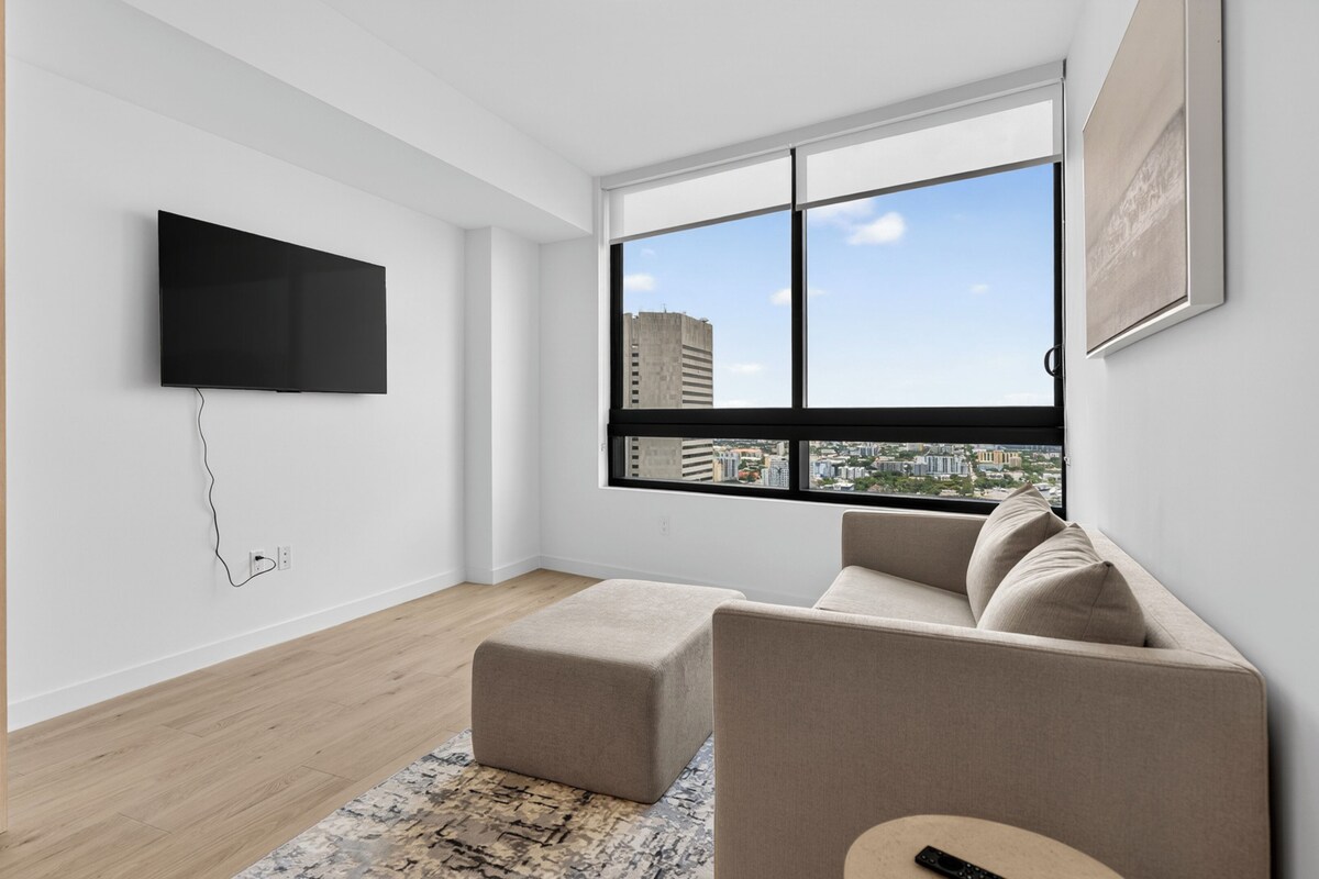 Ein modernes Wohnzimmer mit Flachbildfernseher, einer Couch, einem Couchtisch und einem großen Fenster mit Blick auf die Stadt.