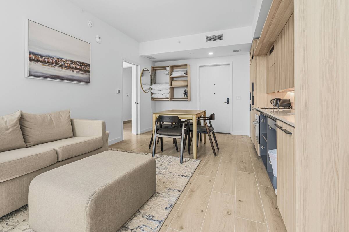 A modern living room with a sofa, ottoman, and a dining area with a table and chairs.