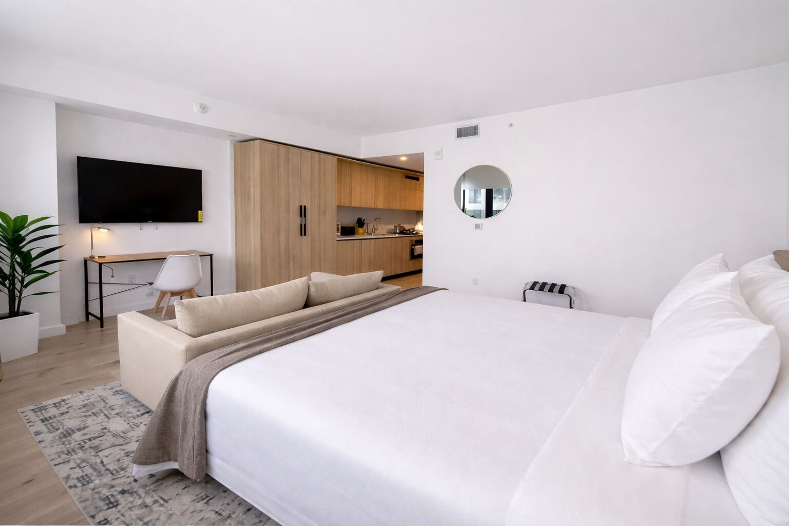 Un dormitorio moderno con una cama grande, un escritorio, una silla, un televisor y una zona de cocina.