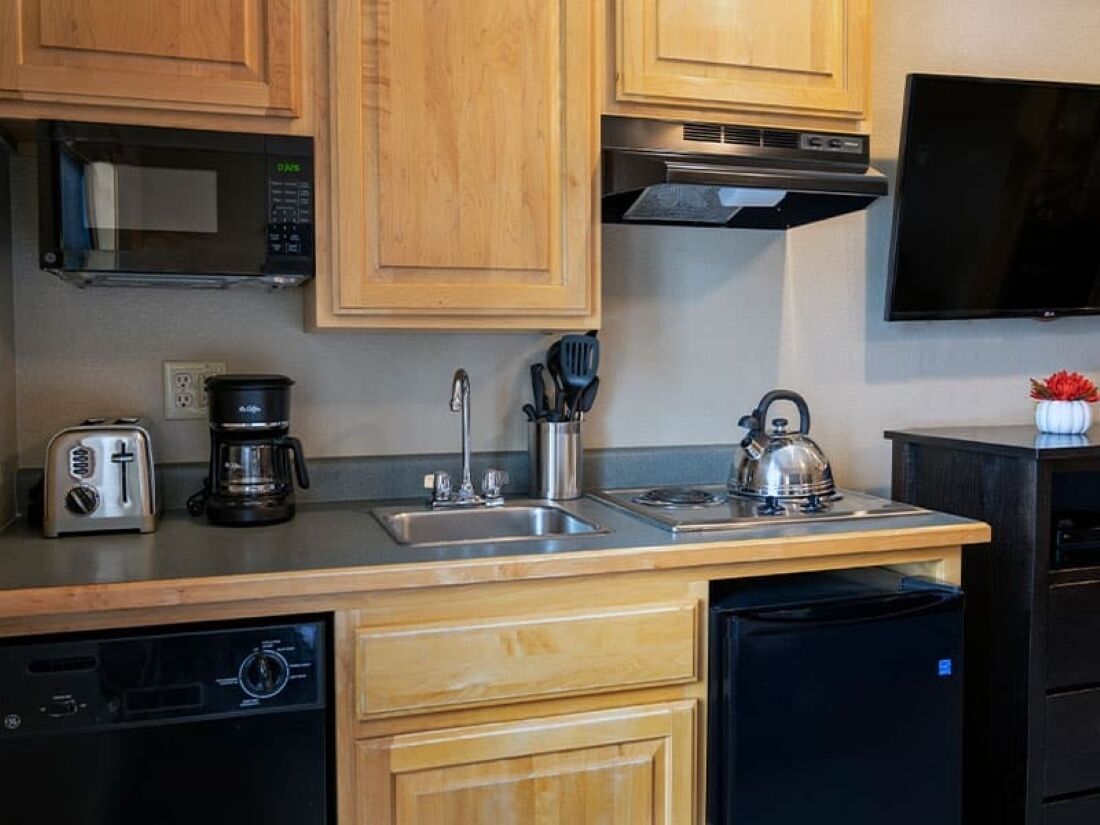 A kitchen with wooden cabinets, a microwave, a coffee maker, a kettle, and a toaster.