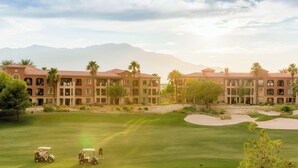 Un parcours de golf doté d’un club-house et d’un bâtiment comportant de nombreux balcons et des palmiers.