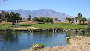 Un parcours de golf avec un étang, des palmiers et des montagnes en arrière-plan.