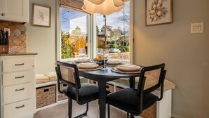 A dining area with a table set for four, chairs, a pendant light, and a view of a building through large windows. - The Ballard Vista | Sleeps 6 + Patio & Fire Pit (Seattle)