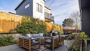 A backyard with a wooden fence, a gray sofa, and a grill. - The Ballard Vista | Sleeps 6 + Patio & Fire Pit (Seattle)