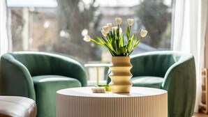 A modern living room with a round, ribbed coffee table in the center, green armchairs, and a view through a large window. - The Ballard Vista | Sleeps 6 + Patio & Fire Pit (Seattle)