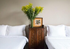 Ein Hotelzimmer mit zwei Betten, einem Nachttisch aus Holz mit einer Vase voller gelber Blumen und einem gerahmten Bild.
