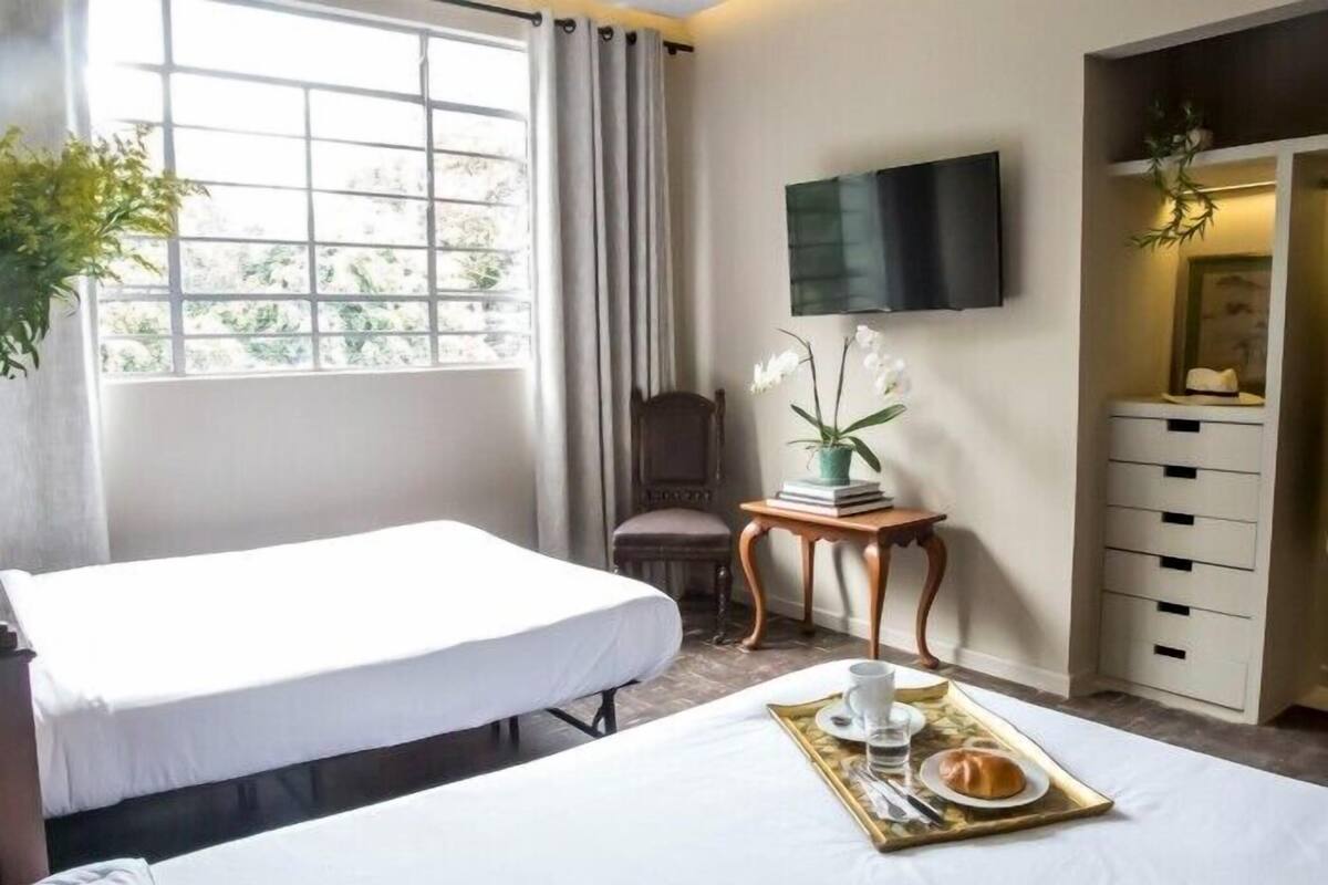 Habitació d'hotel amb dos llits, una televisió, una taula petita amb un plat de desembre, una cadira i una finestra amb cortines.
