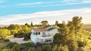 A light-colored two-story house with a balcony, surrounded by dense greenery and trees. - Stunning Escape Hot Tub, Panoramic View, Prime Location Hilltop by Avantstay (Paso Robles)