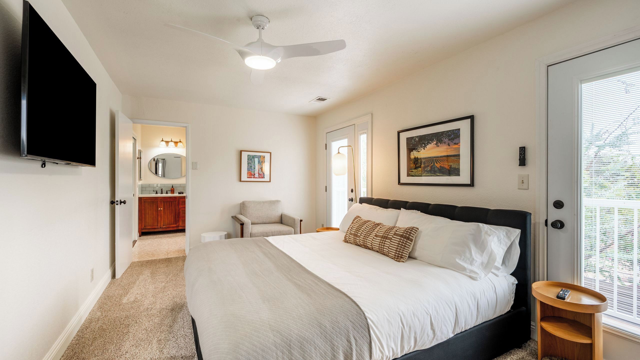 A bedroom with a bed, a chair, a desk, a TV, and a ceiling fan.