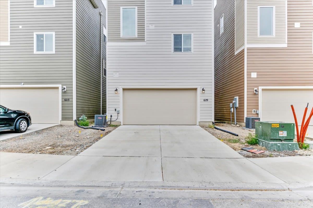 A residential building with a central garage door, two side garages, and a driveway leading to the entrance.