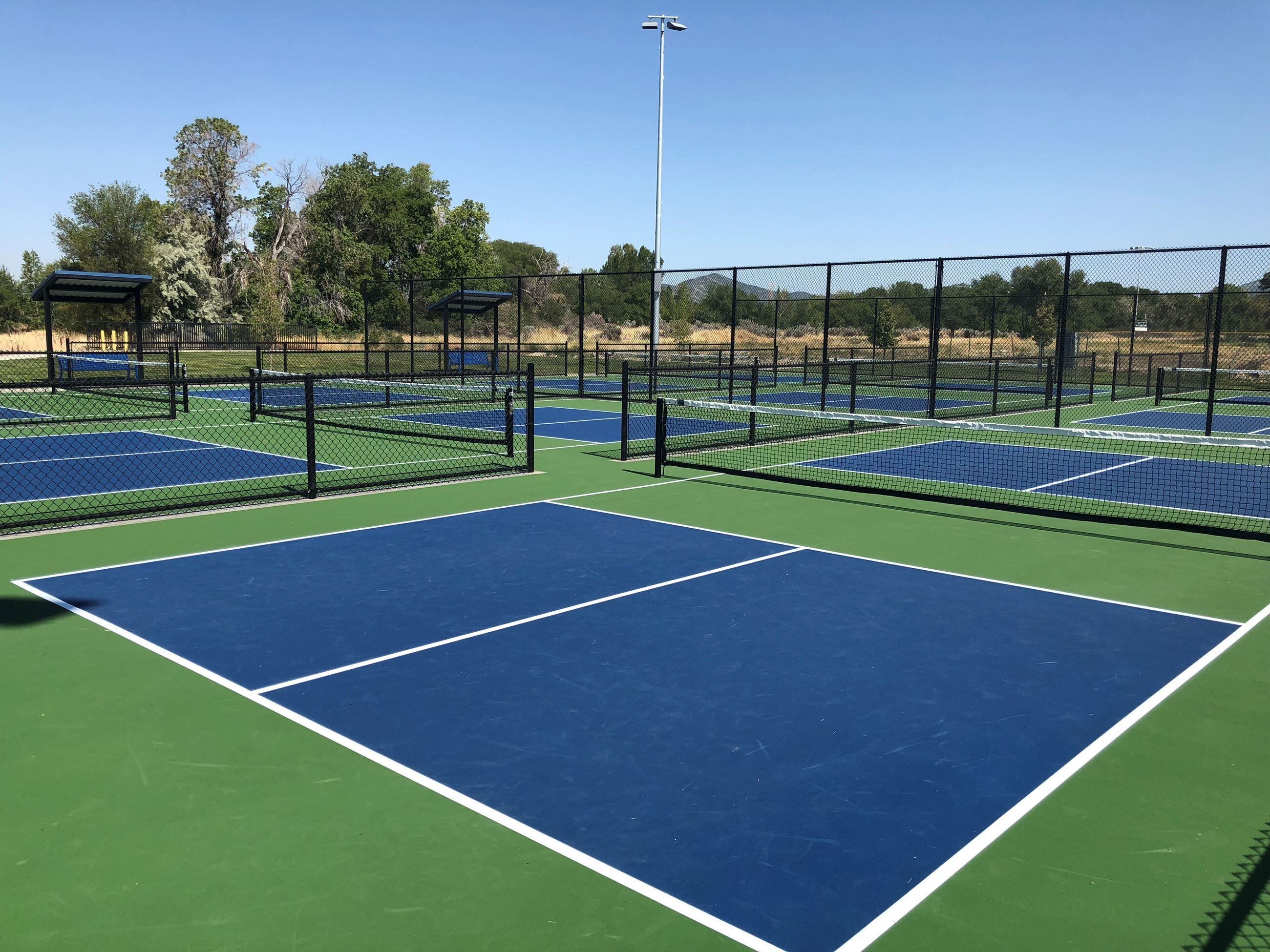 A tennis court with multiple courts, surrounded by a fence, and a covered seating area.