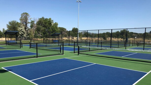 Cancha de tenis con varias pistas, rodeada por una valla y una zona de estar techada.