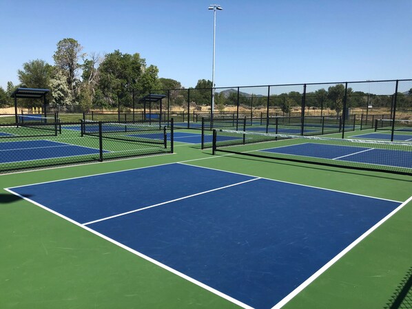 A tennis court with multiple courts, surrounded by a fence, and a covered seating area.