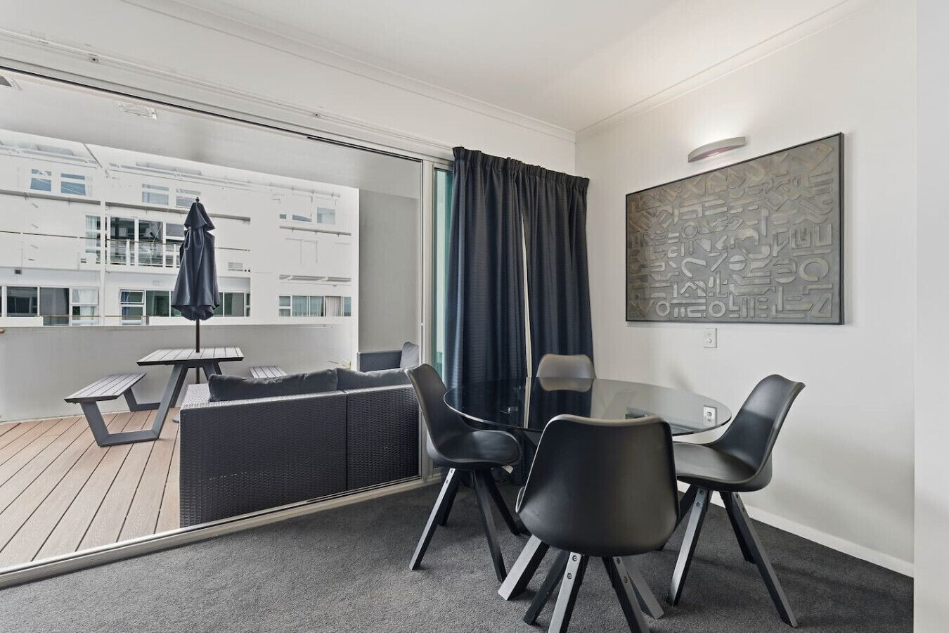 Une pièce moderne comprenant une table à manger, des chaises, un canapé, une petite table avec un banc, et une grande fenêtre avec des rideaux.