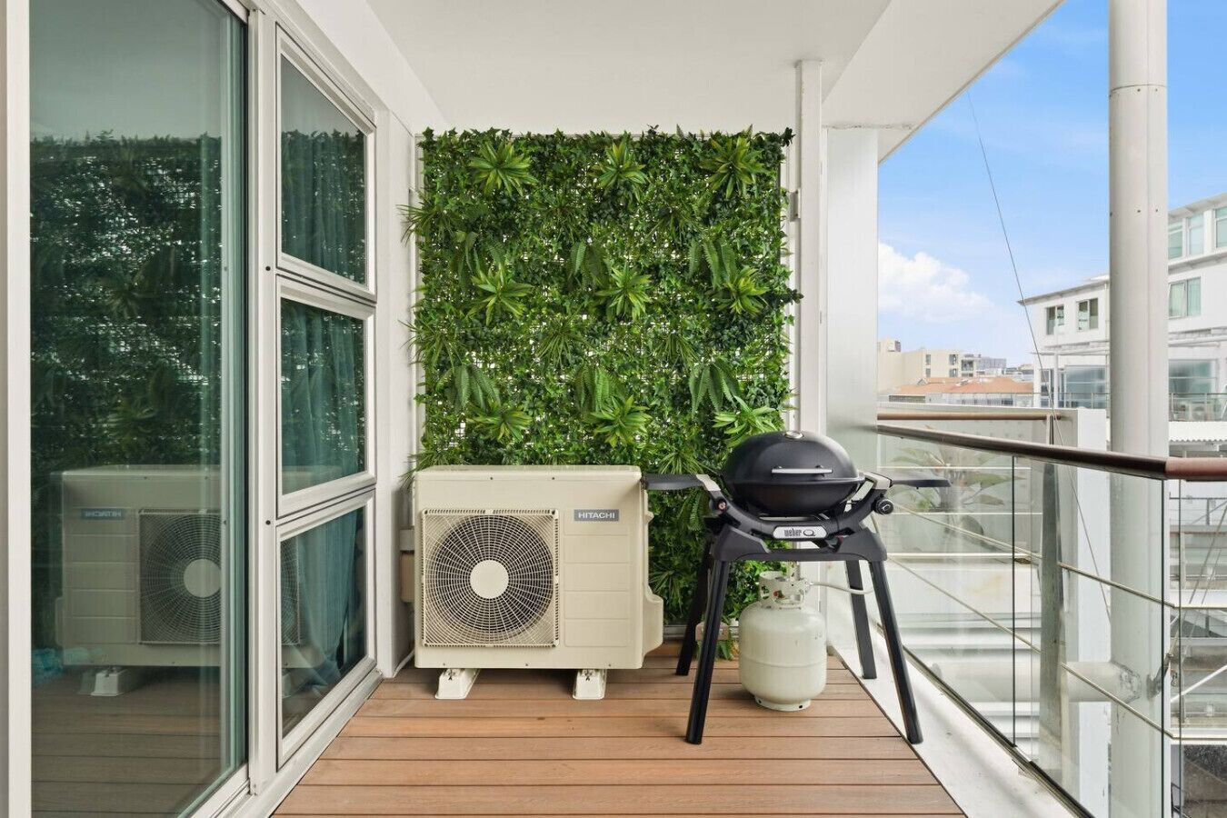 Ein Balkon mit grüner Wand, Klimaanlage und Grill.