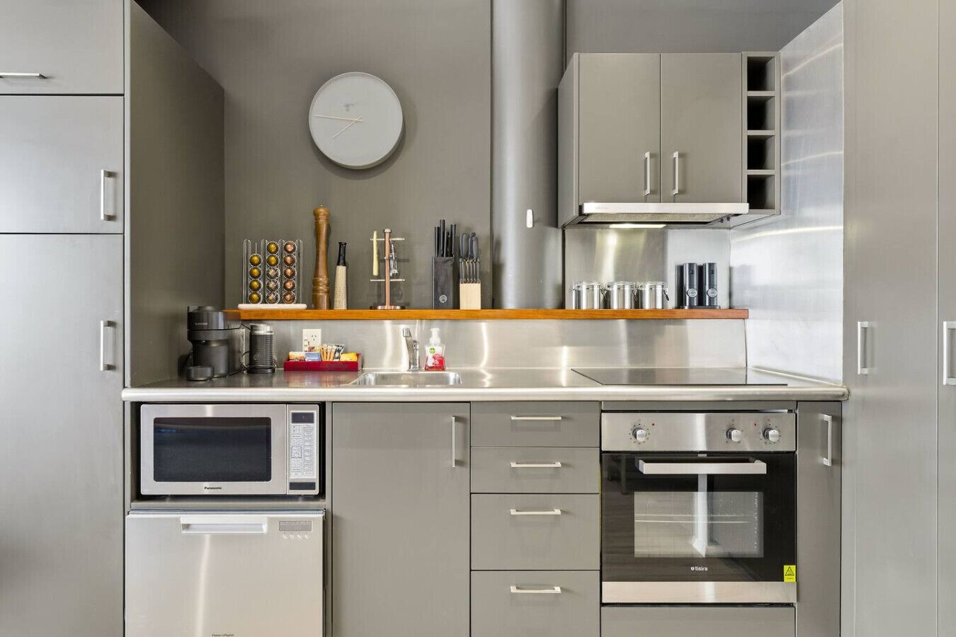 A modern kitchen with stainless steel appliances, a microwave, oven, and a clock on the wall.