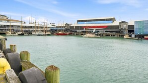 A marina with boats docked, a New Zealand Maritime Museum building, and wooden pilings in the foreground.