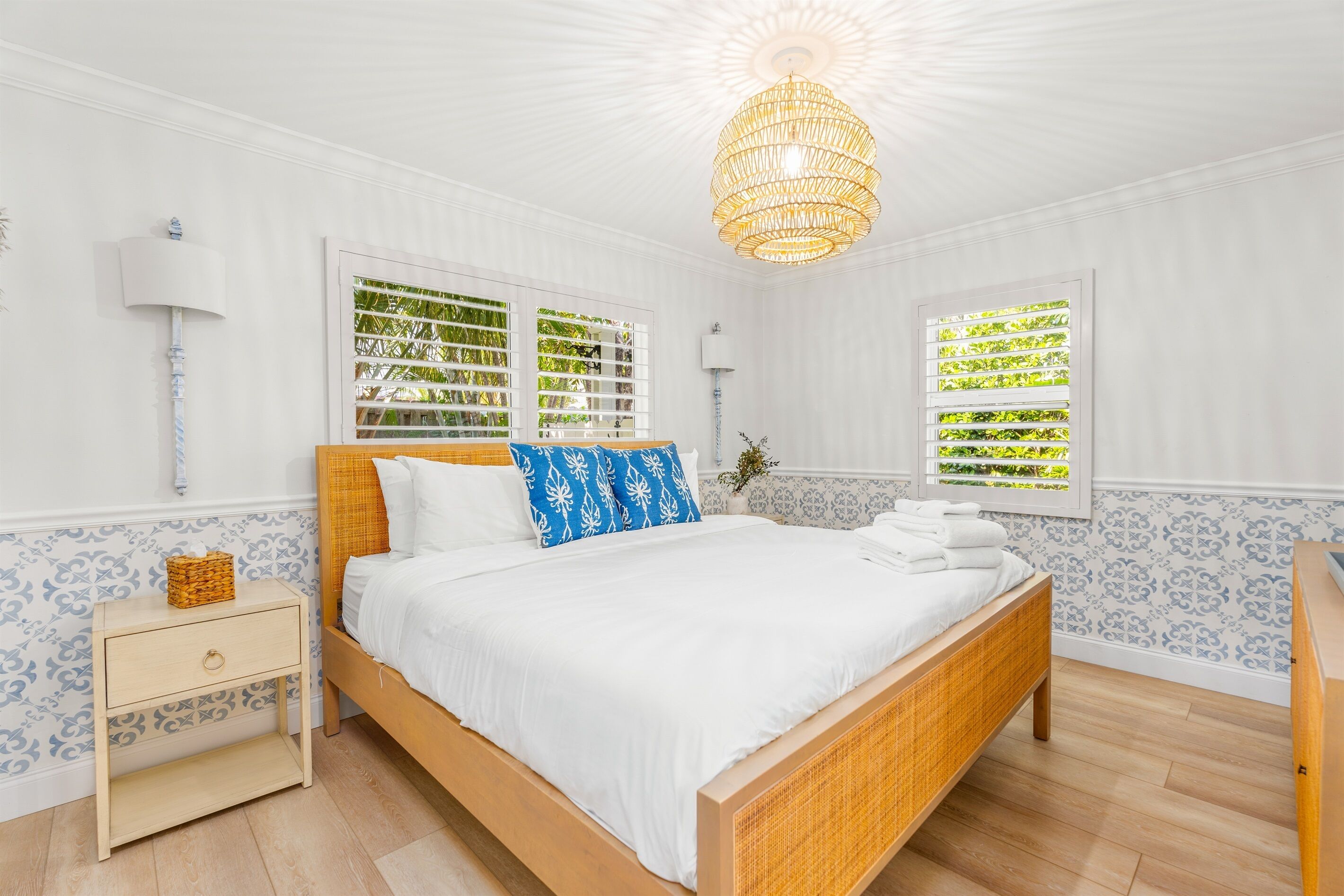 Un dormitorio con una cama de madera, ropa de cama blanca, una mesita de noche y una lámpara colgante.