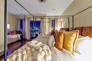 Une chambre d’hôtel moderne avec vue sur la ville, un grand lit agrémenté de plusieurs oreillers, un plaid blanc moelleux et une cloison en verre.