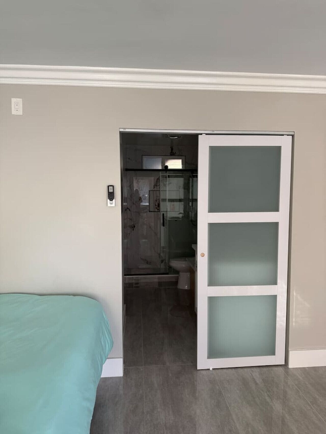 A bedroom with a bed, a bathroom with a toilet and shower, and a sliding door leading to a hallway.
