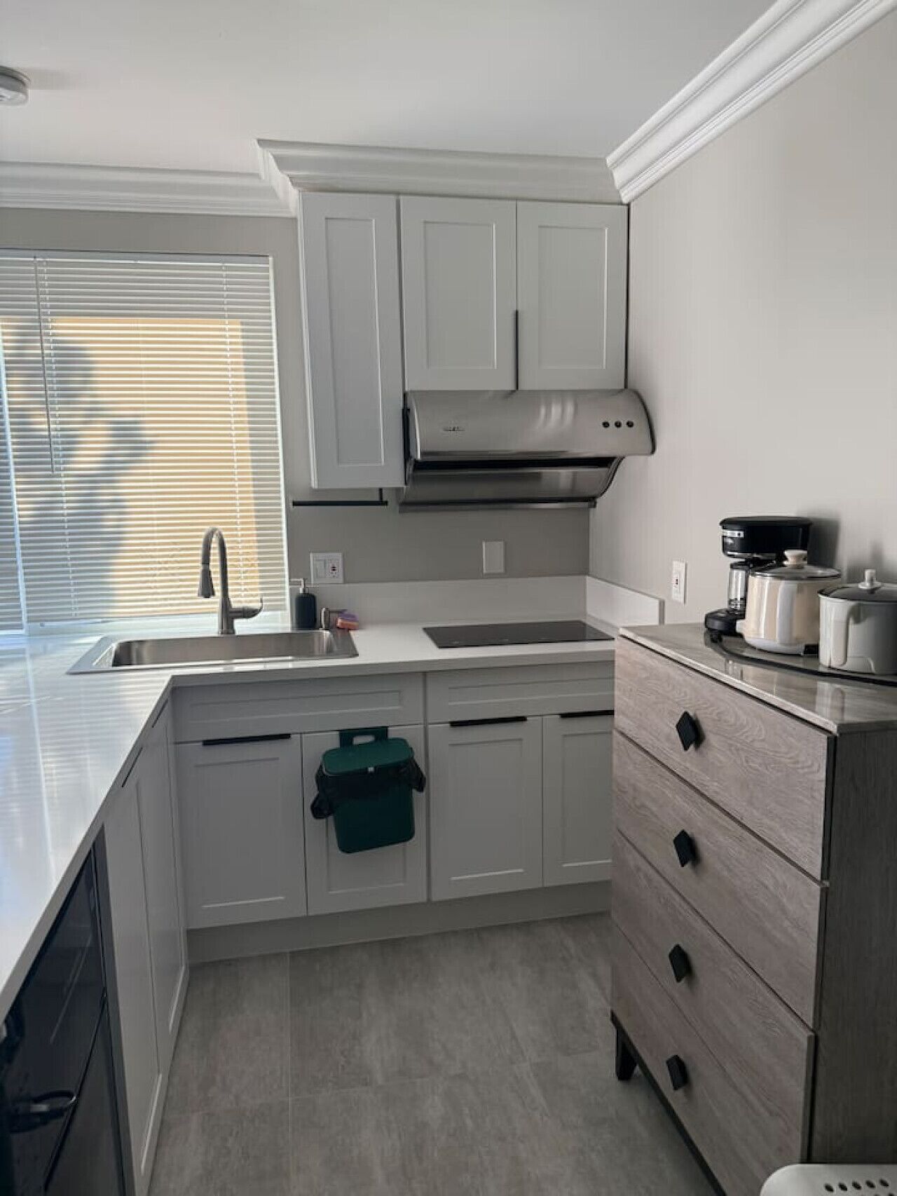 A modern kitchen with white cabinets, a stainless steel range hood, a sink, and a coffee maker.