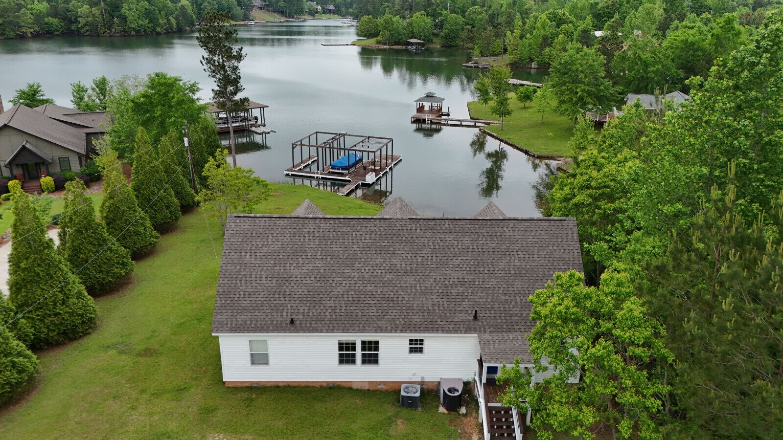 A house with a dock extending into a lake, surrounded by trees and other houses.