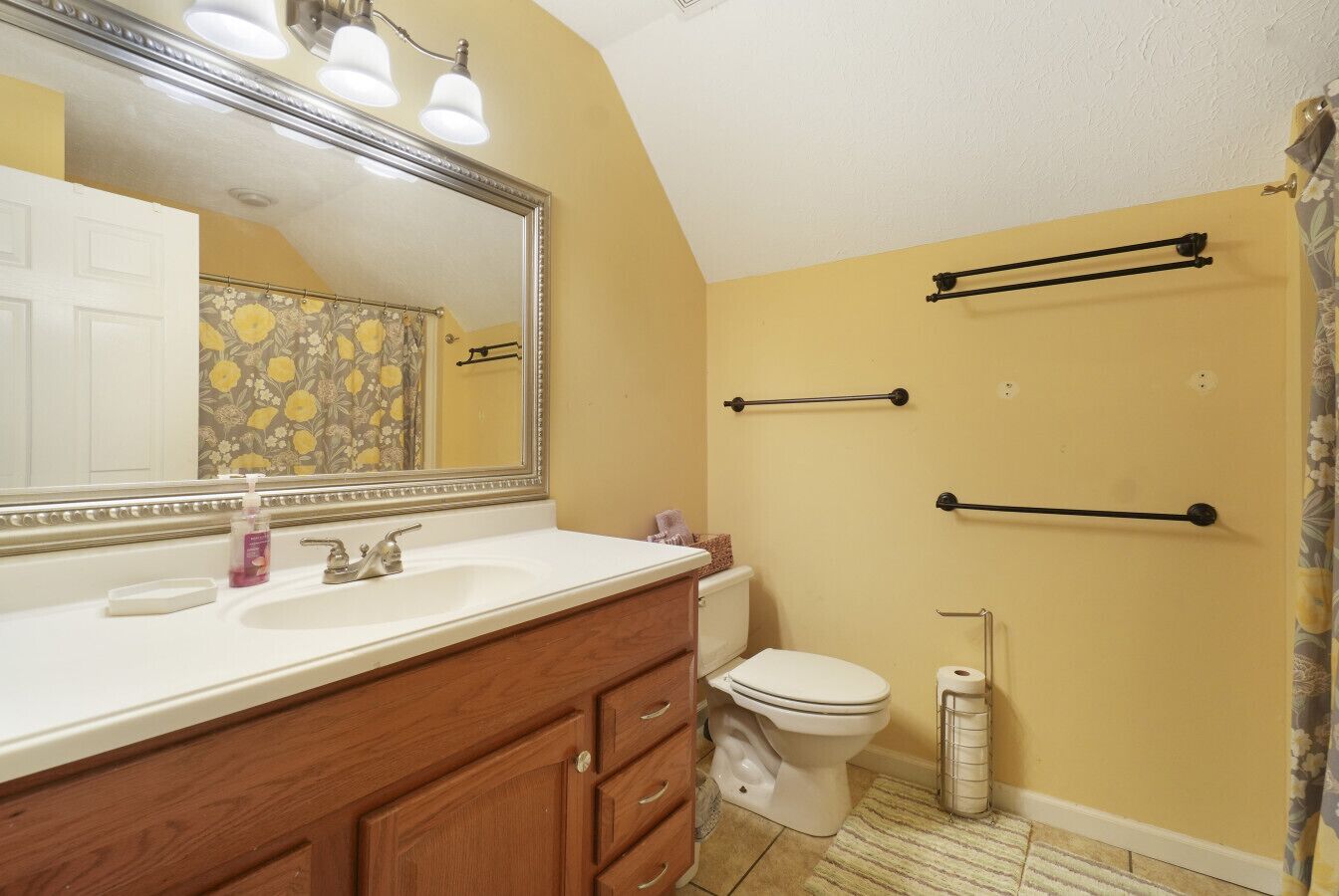 A bathroom with a wooden vanity, a large mirror, a toilet, and towel bars on the wall.