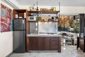 A modern kitchen with a built-in refrigerator, microwave, and sink. There is a dining area with a sofa and a small table. - Cozy Boho Studio in Romantic Zone (Puerto Vallarta)
