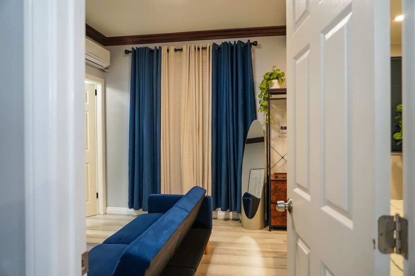 Een kamer met een blauwe bank, beige gordijnen en een spiegel.