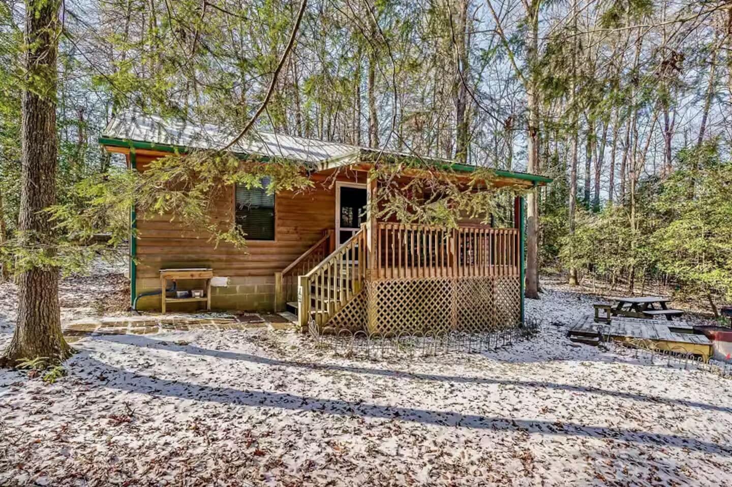 Una cabaña de madera con un porche, una banca y una mesa de picnic en un área boscosa.