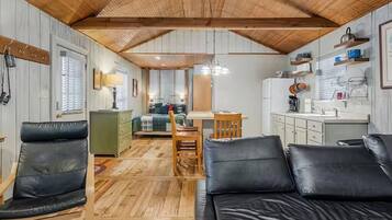 A compact living space with a wooden ceiling, a dining area, a kitchenette, and a sofa.