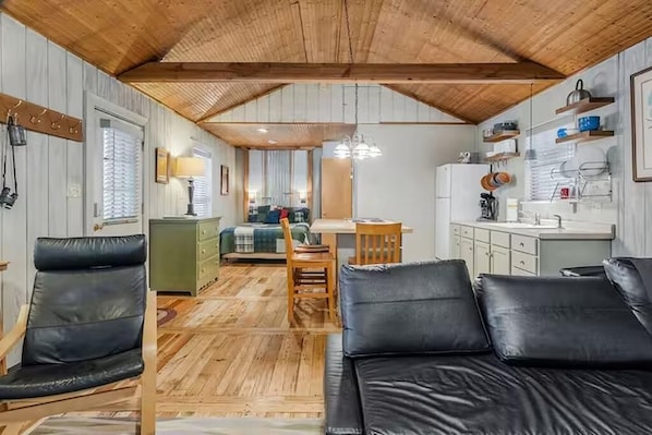 En kompakt opholdsstue med træloft, spiseplads, tekøkken og sofa.