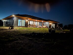 Une cabane en rondins à deux étages, dotée d’un porche couvert et d’un espace extérieur aménagé pour s’asseoir.