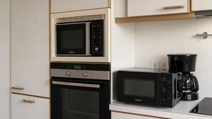 A kitchen with white cabinets, a built-in oven, a microwave, and a coffee maker.