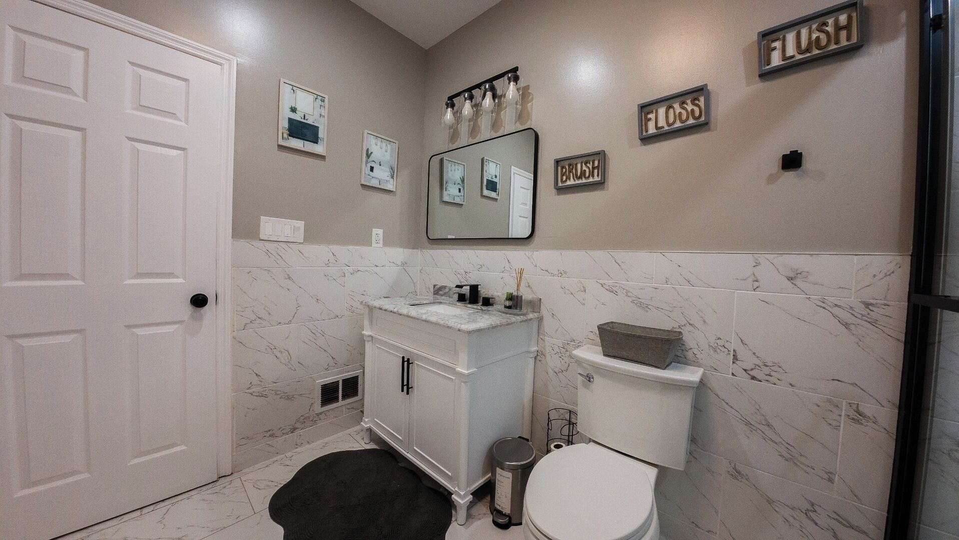 Un baño con puerta blanca, lavamanos de mármol, inodoro y cubo de basura.