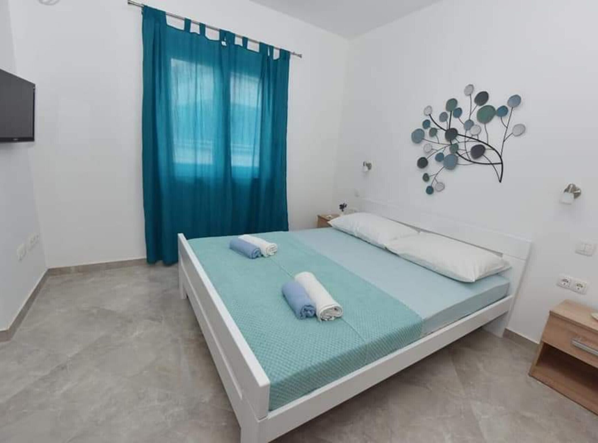 Un dormitorio con cama, una cortina azul, un adorno en la pared y una mesita de noche de madera.