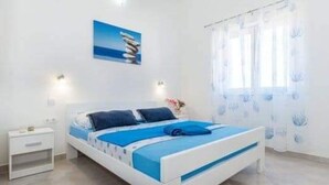 Un dormitorio con cama, mesita de noche, lámpara de pared y ventana con cortinas.