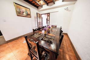 A dining area with a wooden table and chairs, a painting on the wall, and a view through an open door. - Los Faroles Hotel & Spa (Antigua Guatemala)