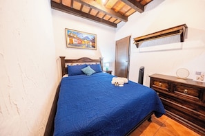 A bedroom with a bed, a wooden dresser, a painting on the wall, and a door. - Los Faroles Hotel & Spa (Antigua Guatemala)