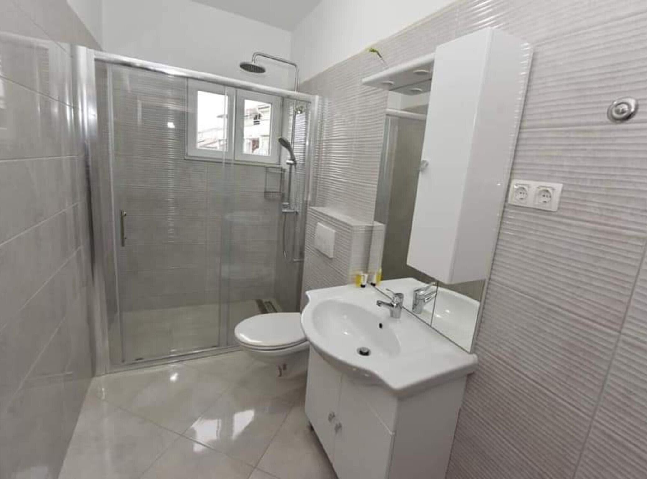 Une salle de bain moderne avec une douche à parois de verre, un lavabo blanc et un grand miroir.