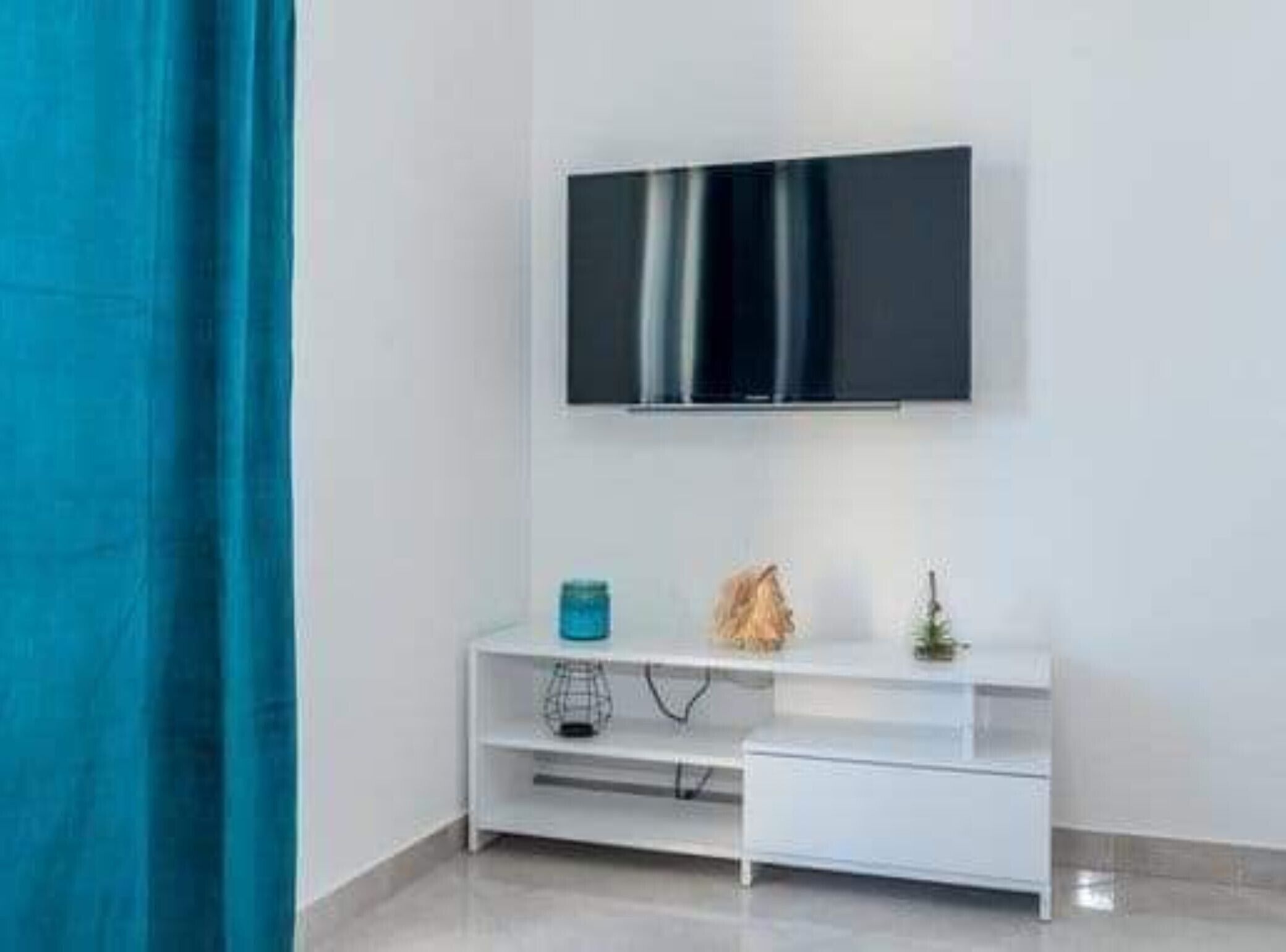 A modern room with a mounted TV on the wall, a white console table, and a blue curtain.