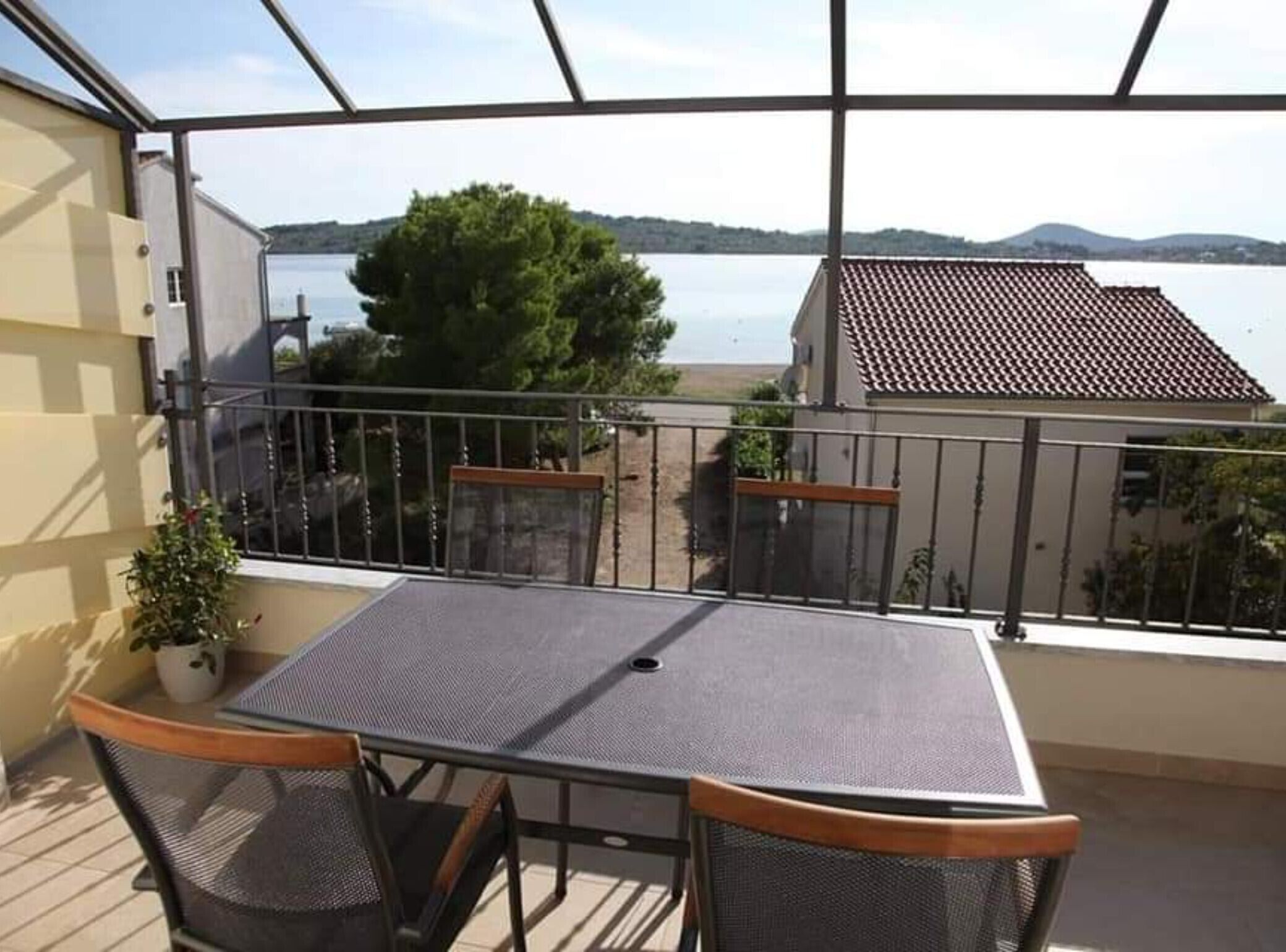 Een balkon met een tafel en stoelen, met uitzicht op een meer en een gebouw met een pannendak.