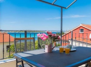 A balcony with a table, a vase of flowers, and two glasses of orange juice. - Apartments Ana - Studio apartment (Srima)