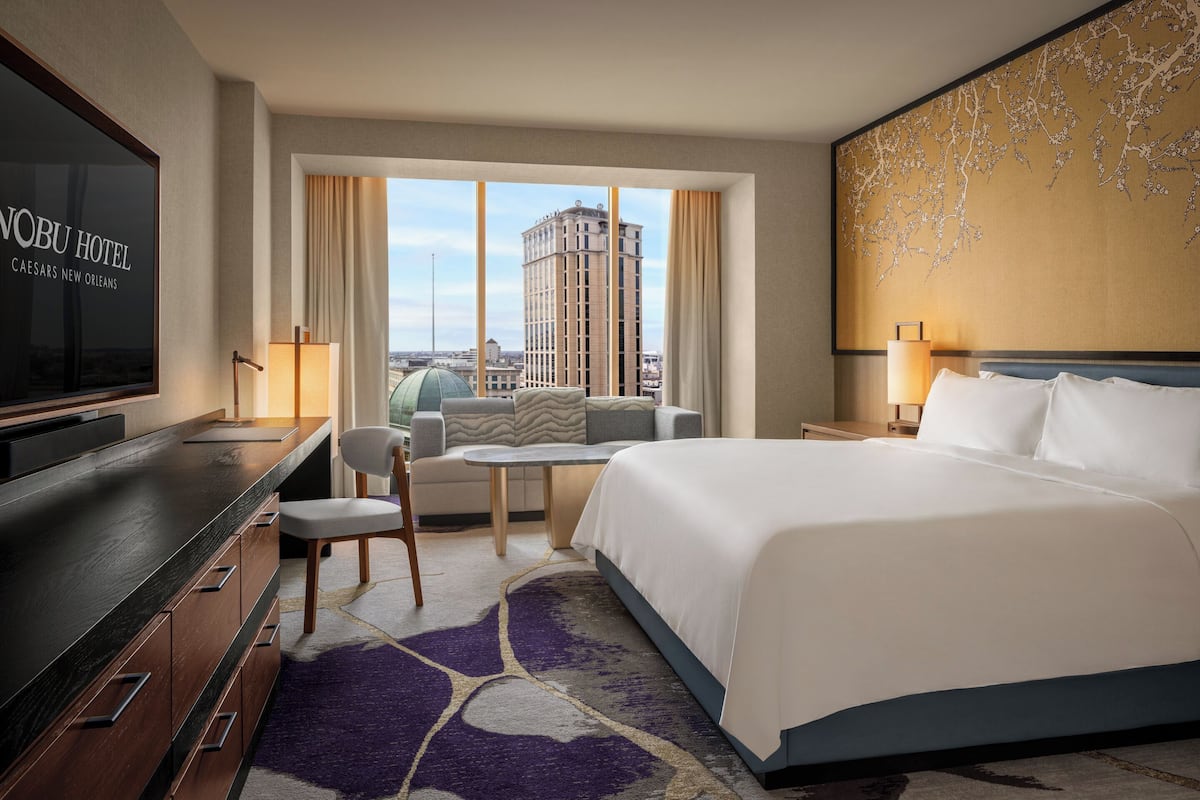 A hotel room with a bed, a TV, a sofa, a small table, and a view of the city.