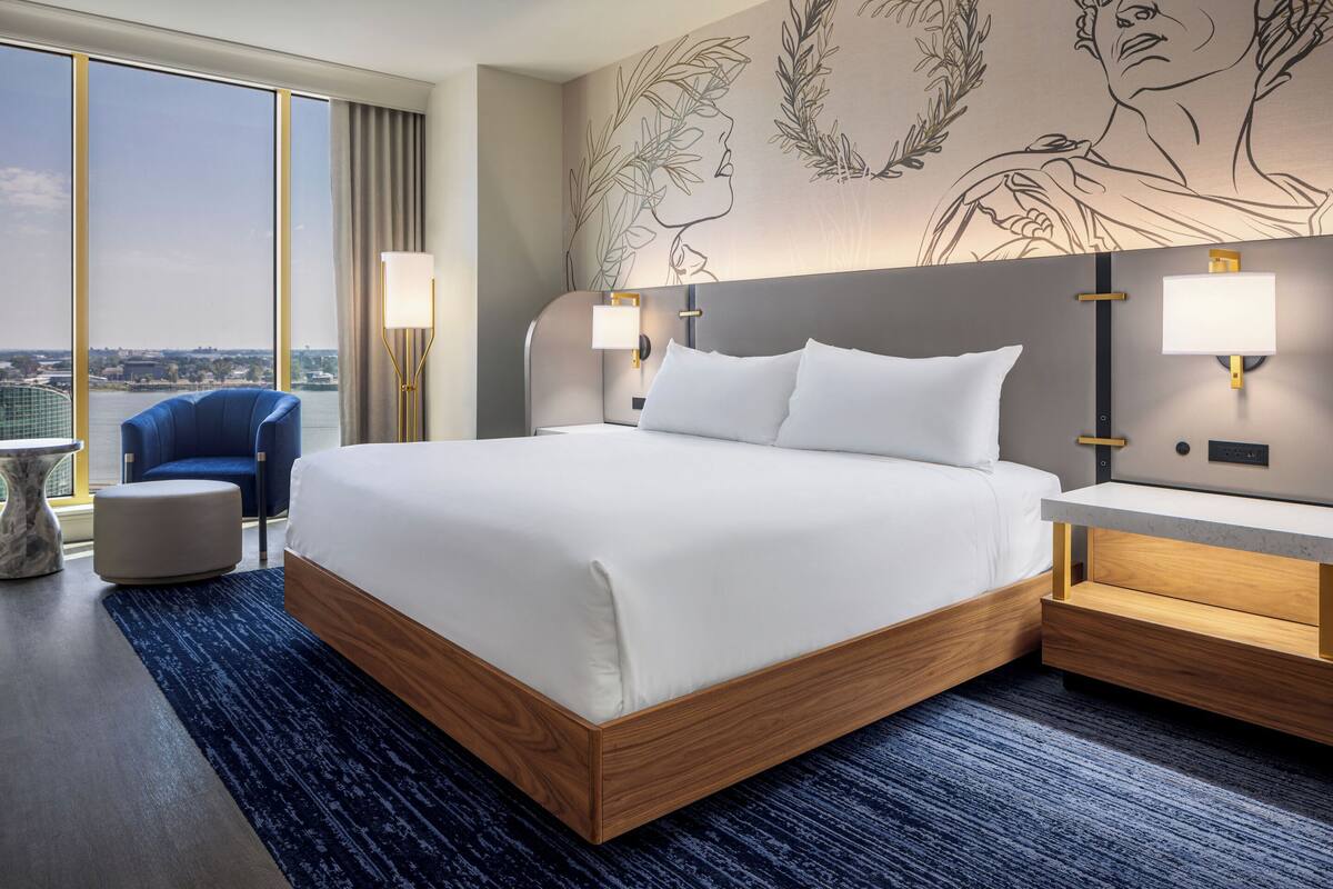 A hotel room with a large bed, bedside lamps, a chair, and a view of the city.